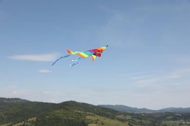 One colorful kite flying in mountains under blue sky