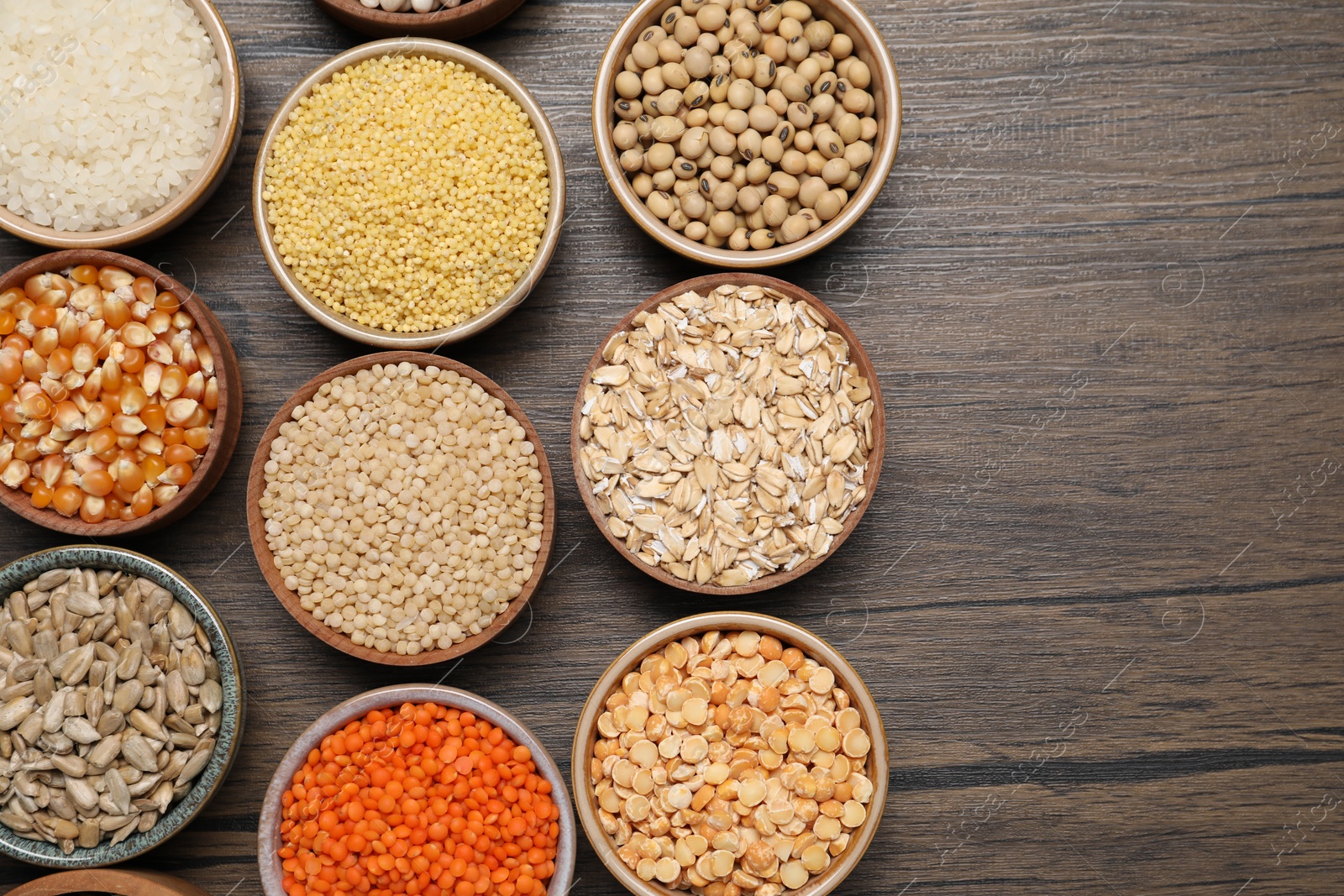 Photo of Different types of cereals, seeds and legumes in bowls on wooden table, flat lay. Space for text