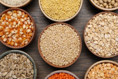 Photo of Different types of cereals, seeds and legumes in bowls on wooden table, flat lay