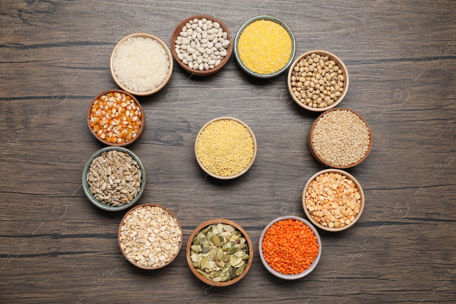 Photo of Different types of cereals, seeds and legumes in bowls on wooden table, flat lay