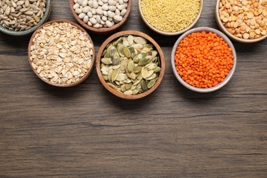 Photo of Different types of cereals, seeds and legumes in bowls on wooden table, flat lay. Space for text