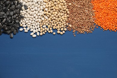 Photo of Different types of cereals, legumes and seeds on blue wooden table, flat lay. Space for text