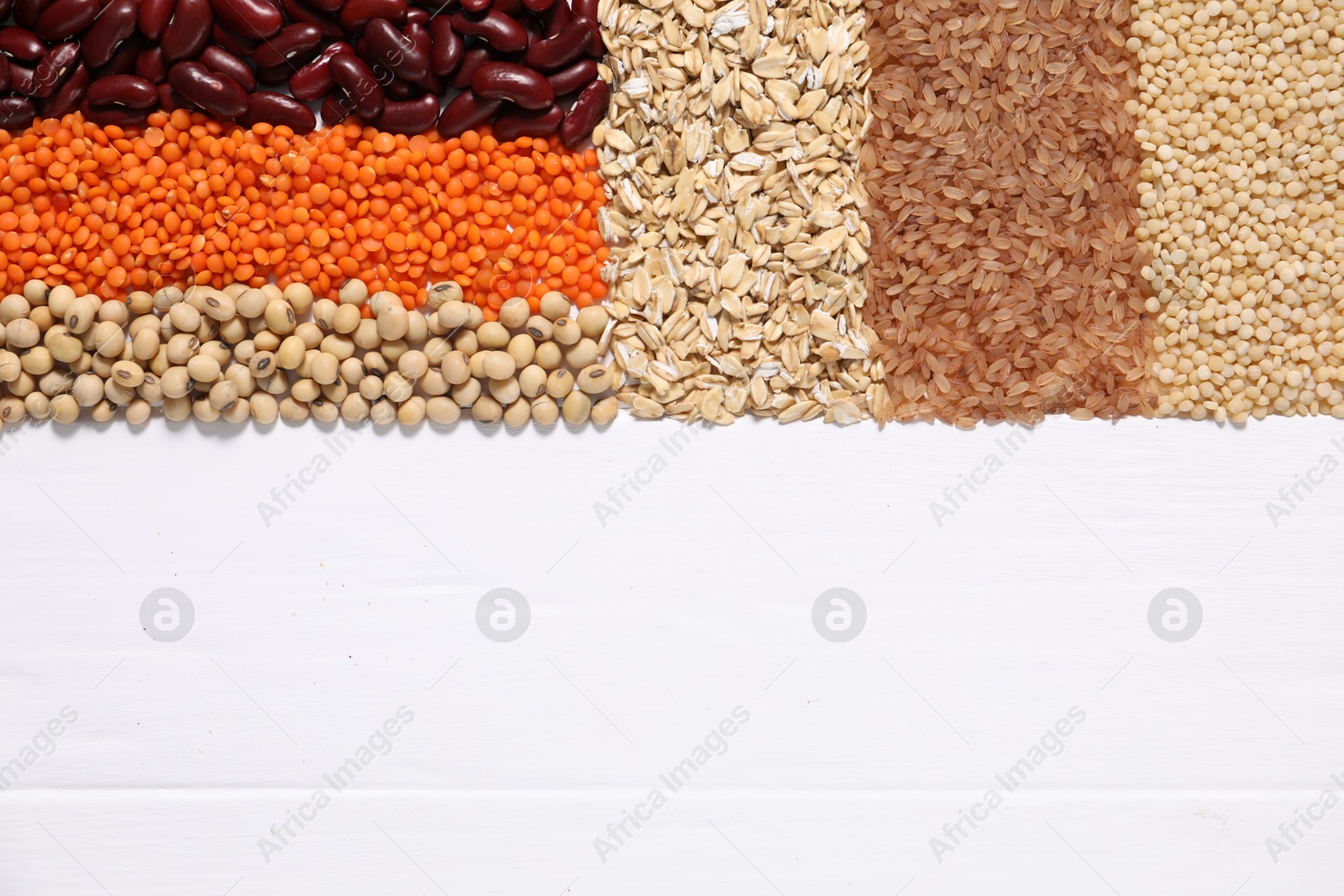 Photo of Different types of cereals and legumes on white wooden table, flat lay. Space for text