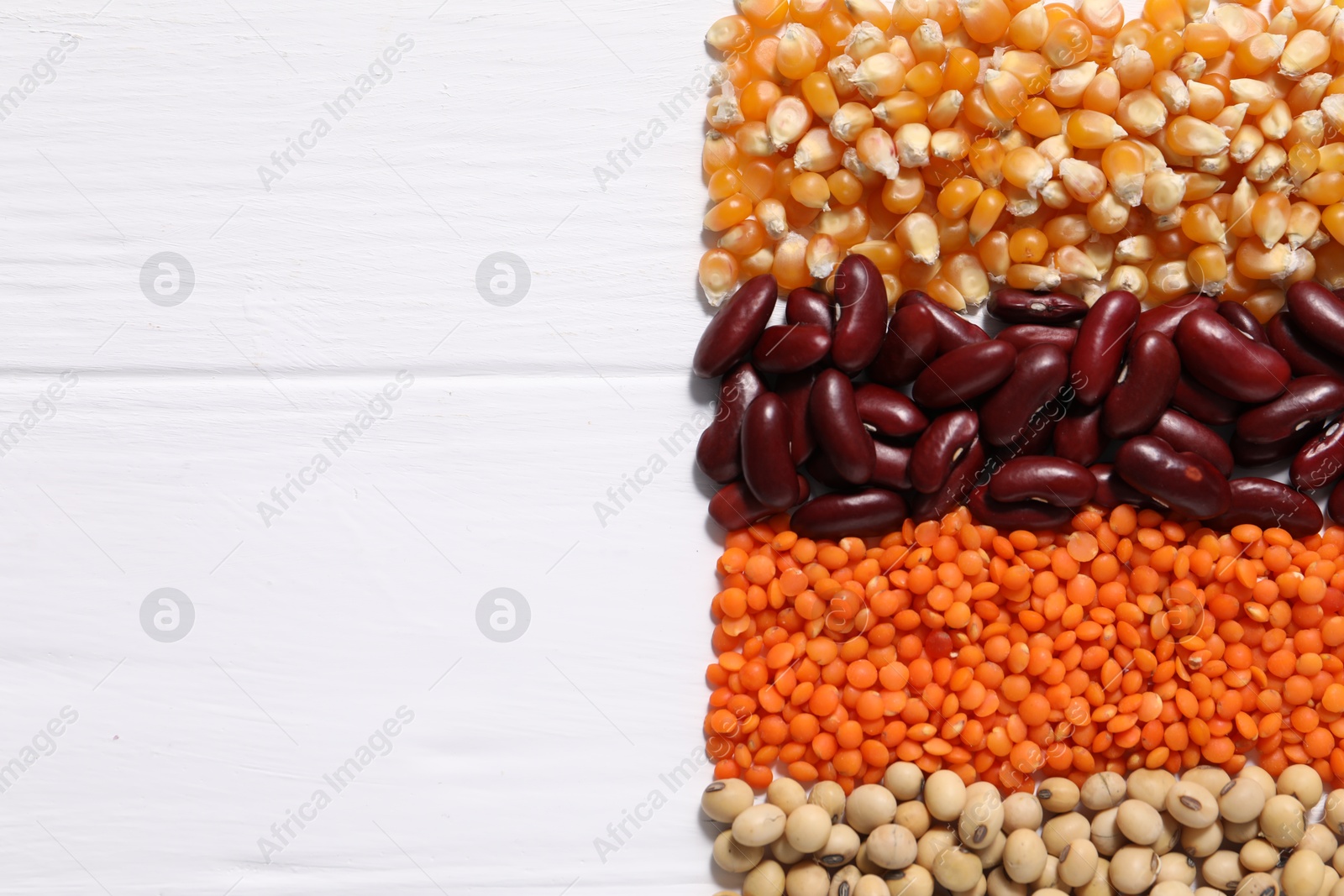 Photo of Different types of legumes on white wooden table, flat lay. Space for text