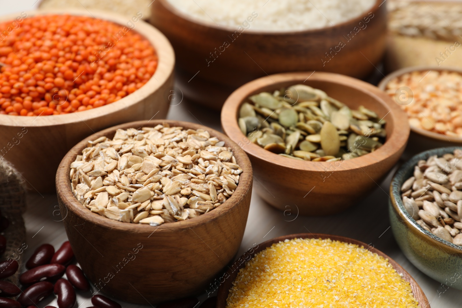 Photo of Different types of legumes, seeds and cereals in bowls on white table, closeup