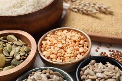 Photo of Different types of seeds and cereals in bowls on white table, closeup