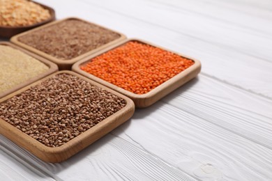 Photo of Different types of cereals and legumes on white wooden table, closeup. Space for text