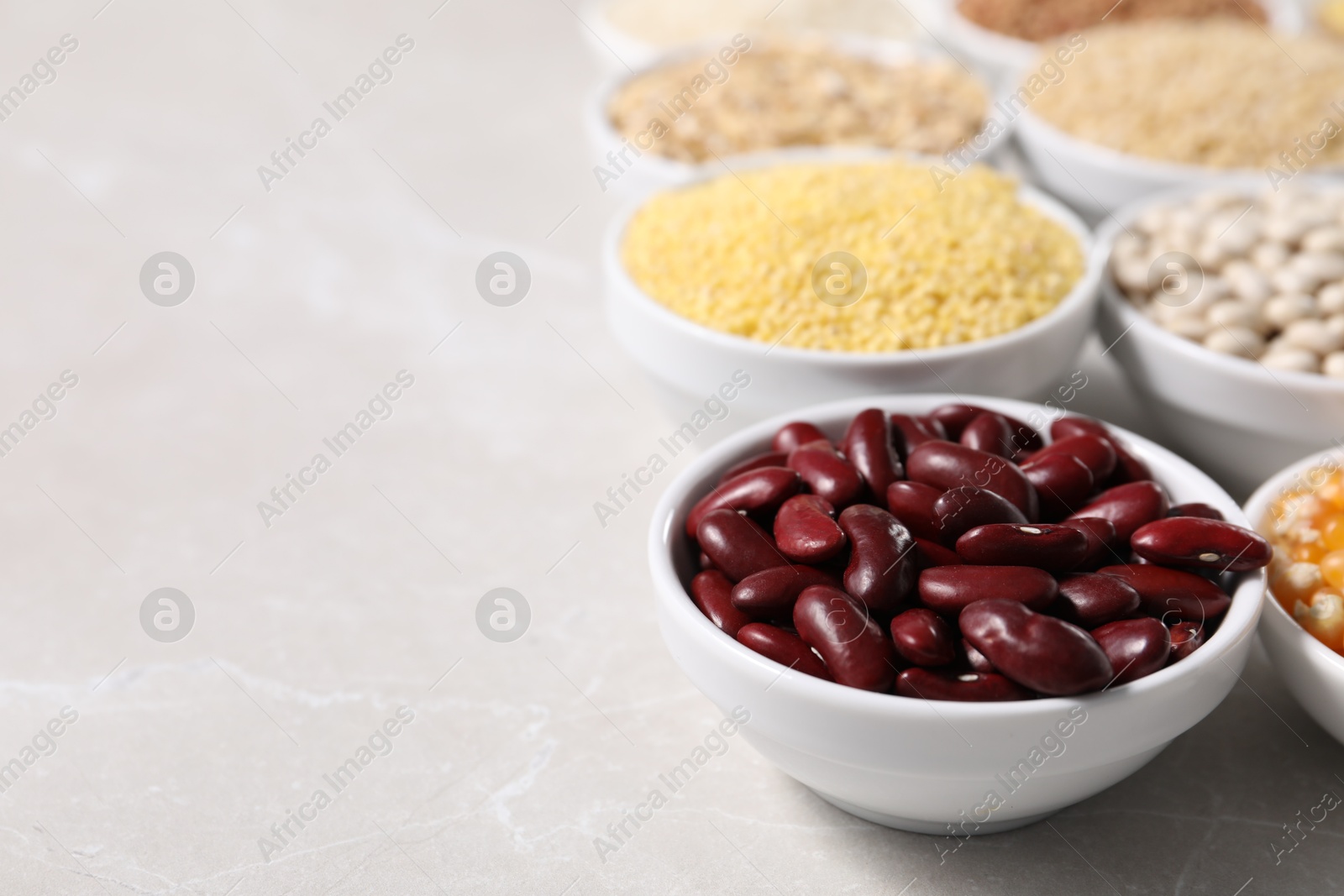 Photo of Different types of legumes and cereals in bowls on light marble table, closeup. Space for text