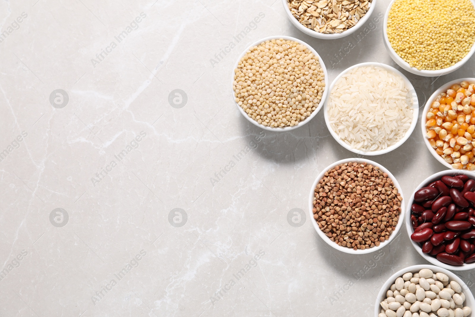 Photo of Different types of legumes and cereals in bowls on light marble table, flat lay. Space for text