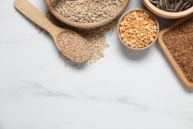 Photo of Different types of seeds and cereals on white marble table, flat lay. Space for text