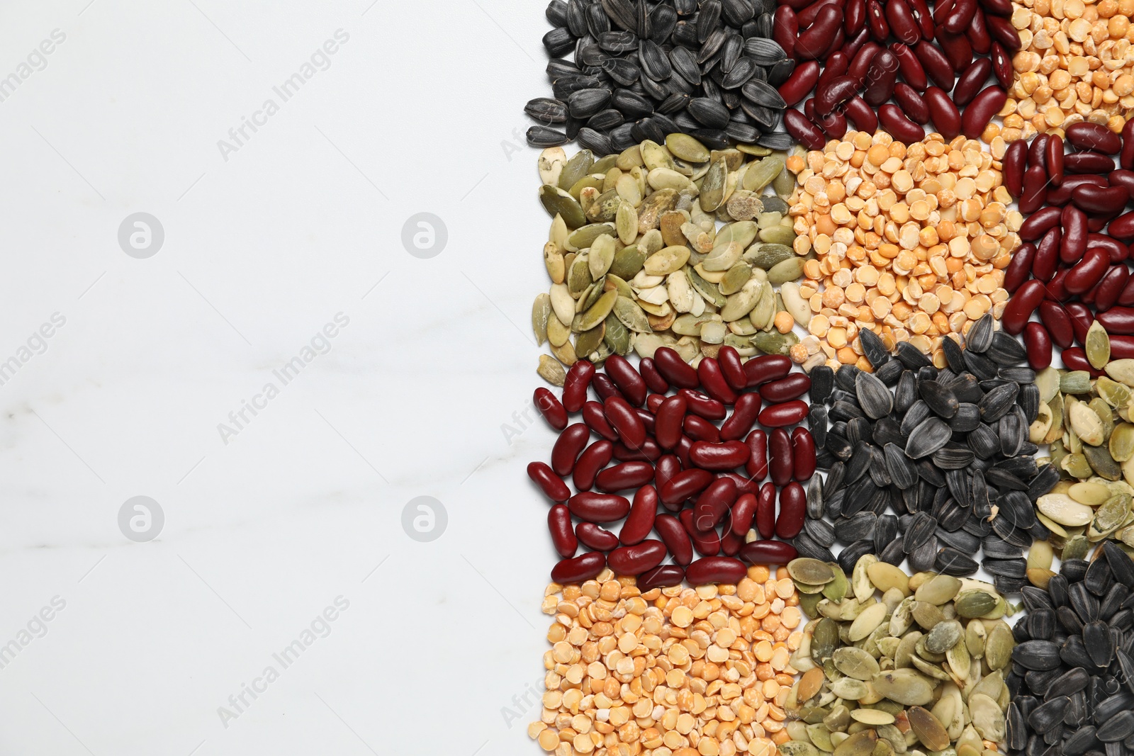 Photo of Different types of legumes and seeds on white marble table, top view. Space for text