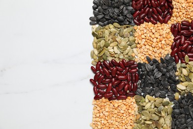 Photo of Different types of legumes and seeds on white marble table, top view. Space for text