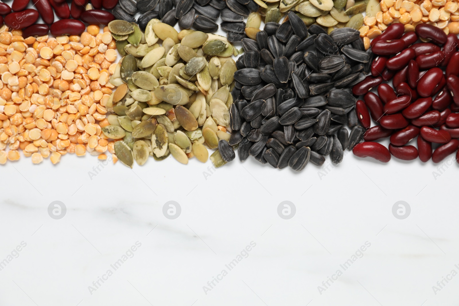 Photo of Different types of legumes and seeds on white marble table, top view. Space for text