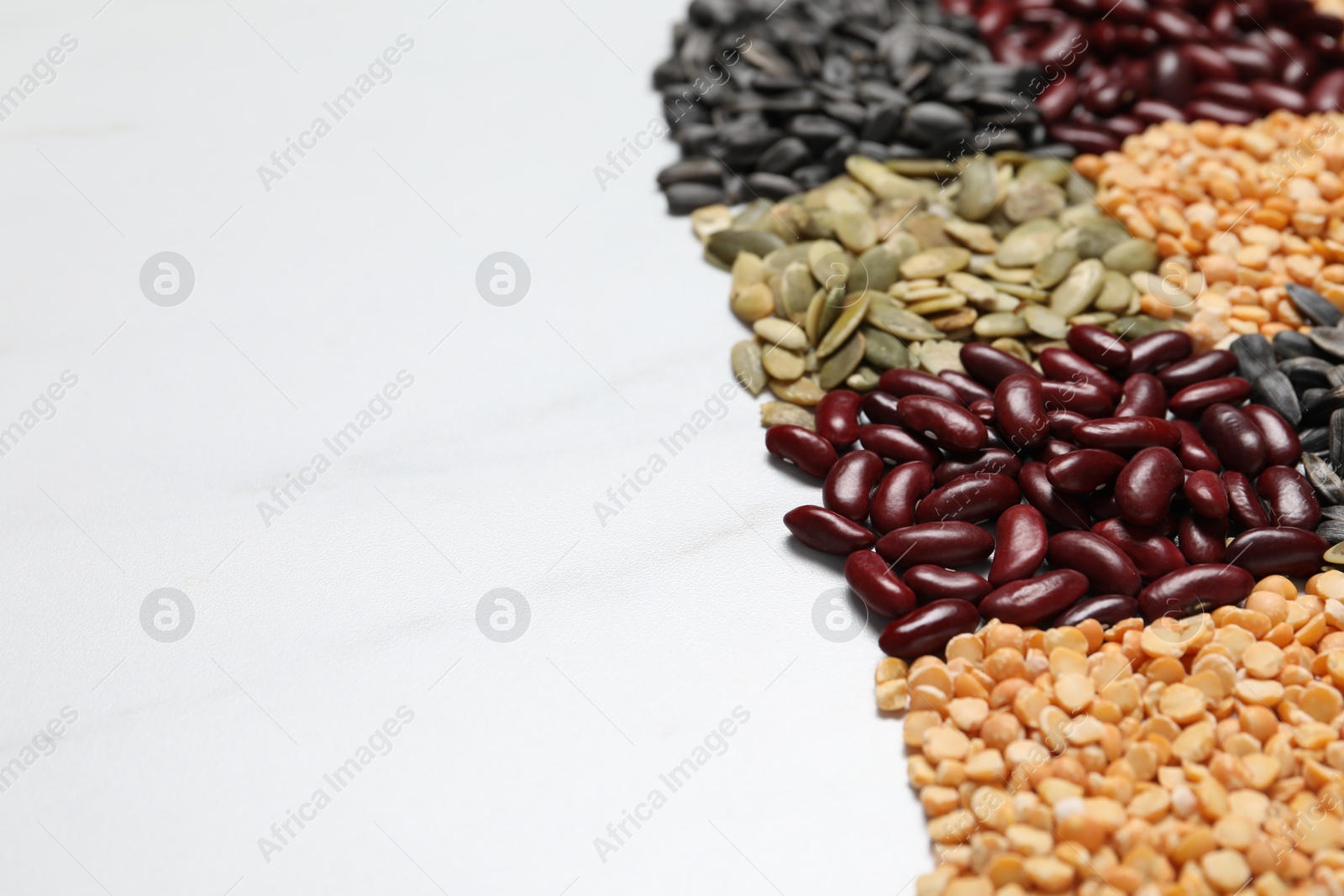 Photo of Different types of legumes and seeds on white marble table, closeup. Space for text