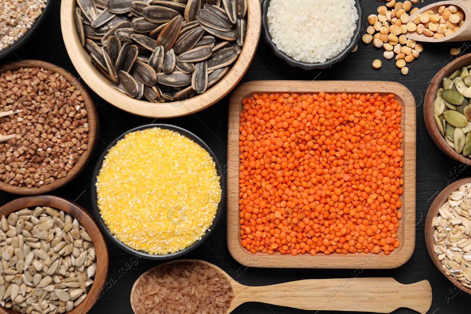 Photo of Different types of legumes, seeds and cereals on black wooden table, flat lay