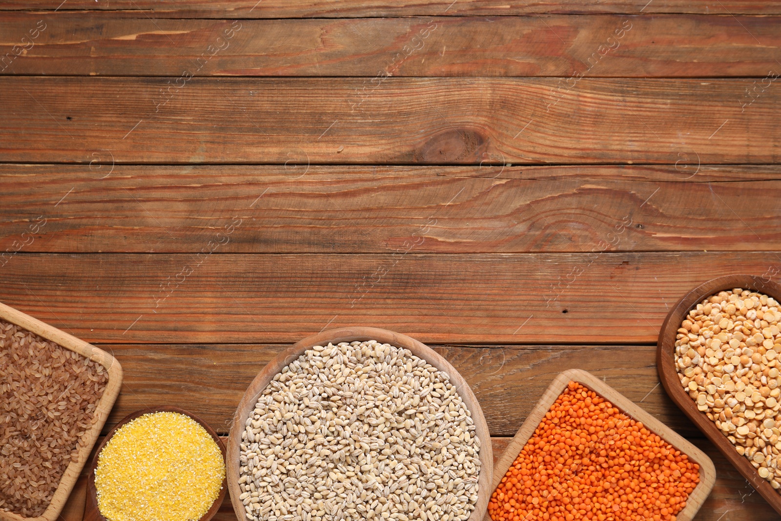 Photo of Different types of cereals and legumes on wooden table, flat lay. Space for text