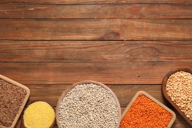 Photo of Different types of cereals and legumes on wooden table, flat lay. Space for text