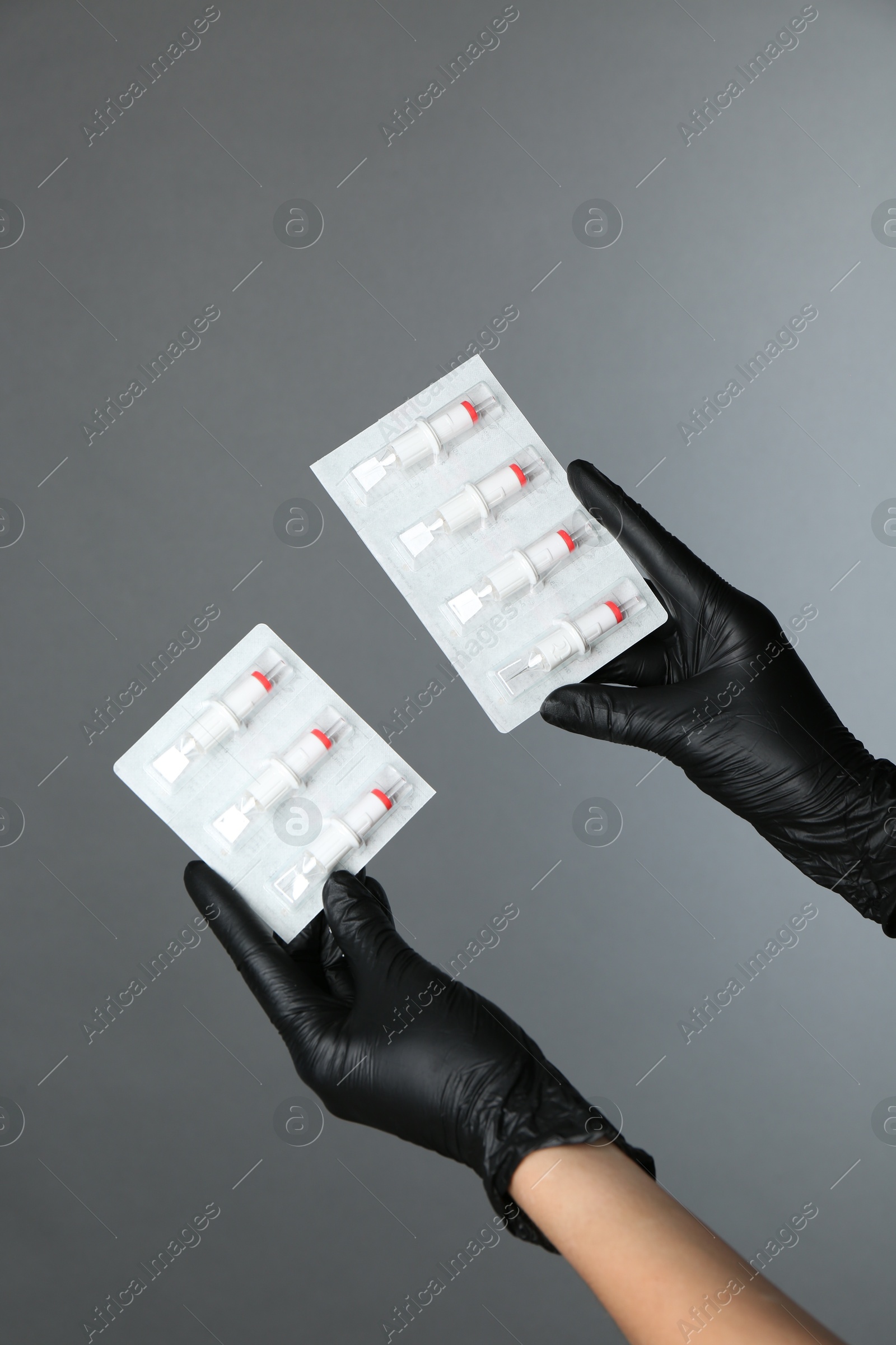 Photo of Professional cosmetologist holding disposable cartridge systems for permanent makeup on grey background, closeup