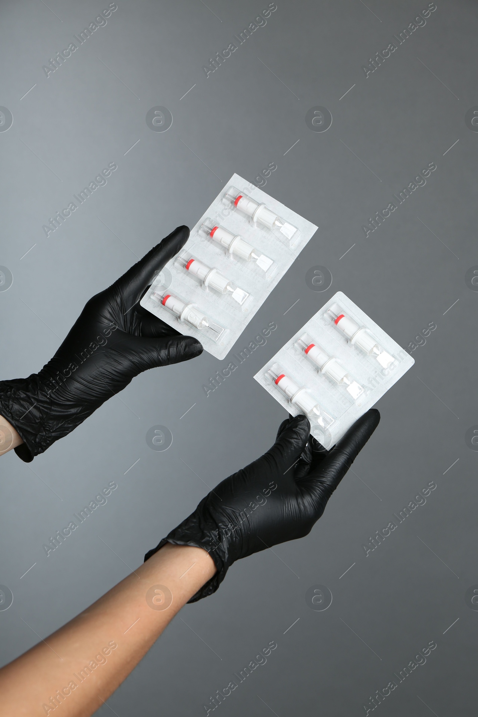 Photo of Professional cosmetologist holding disposable cartridge systems for permanent makeup on grey background, closeup