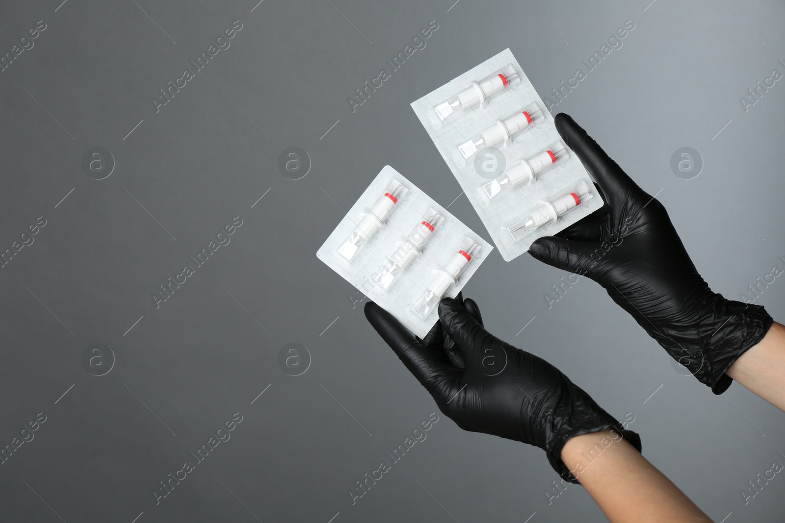 Photo of Professional cosmetologist holding disposable cartridge systems for permanent makeup on grey background, closeup. Space for text