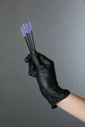 Professional cosmetologist holding disposable makeup brushes on grey background, closeup