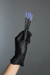 Professional cosmetologist holding disposable makeup brushes on grey background, closeup