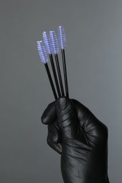 Photo of Professional cosmetologist holding disposable makeup brushes on grey background, closeup