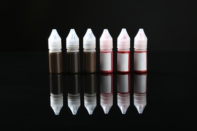 Photo of Bottles of pigments for permanent makeup on black mirror surface