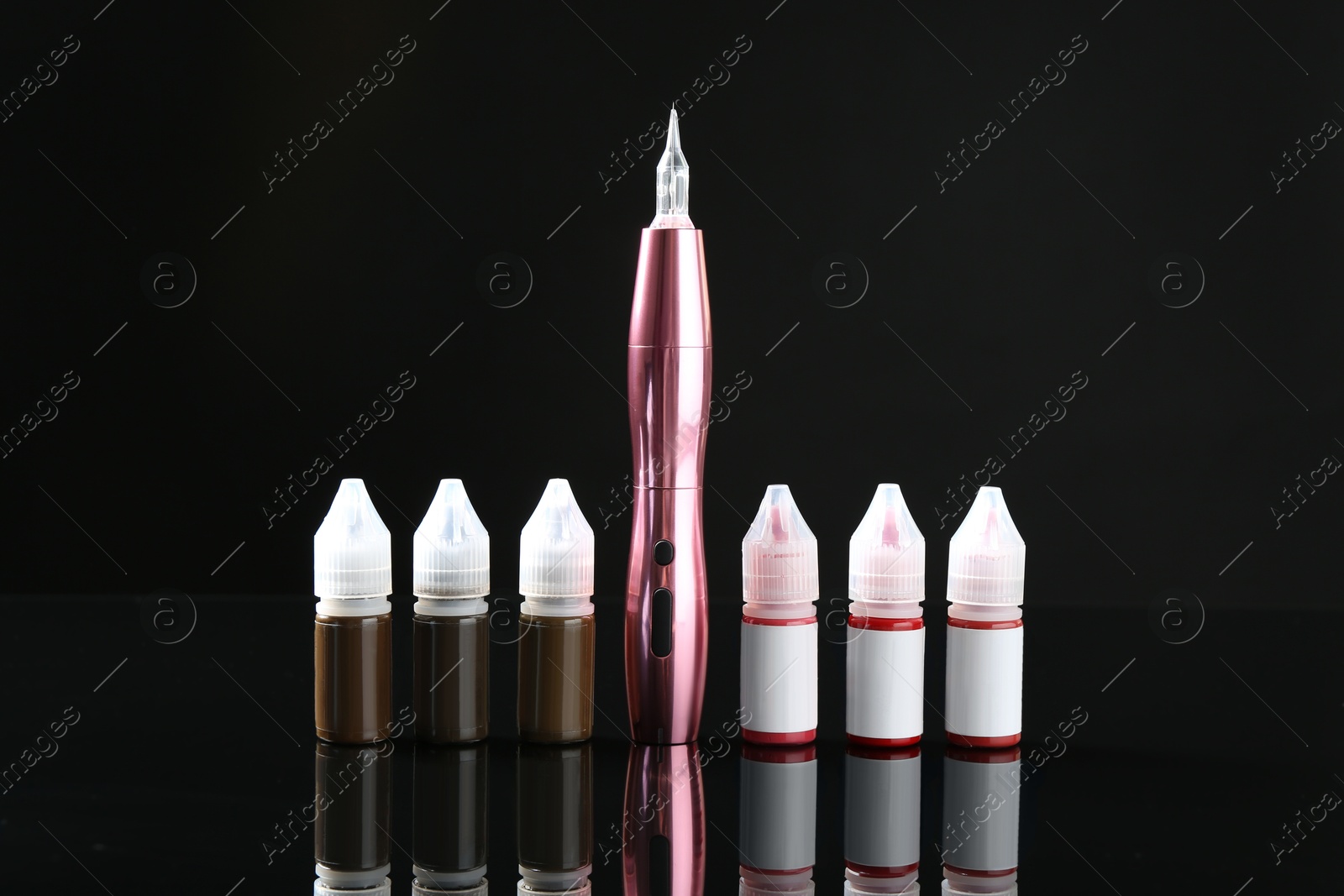 Photo of Professional permanent makeup machine and bottles of pigments on black mirror surface