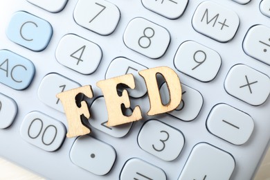 Photo of Wooden letters Fed (Federal Reserve System) and calculator on white table, flat lay