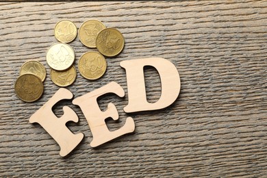 Photo of Letters Fed (Federal Reserve System) and coins on wooden table, flat lay. Space for text