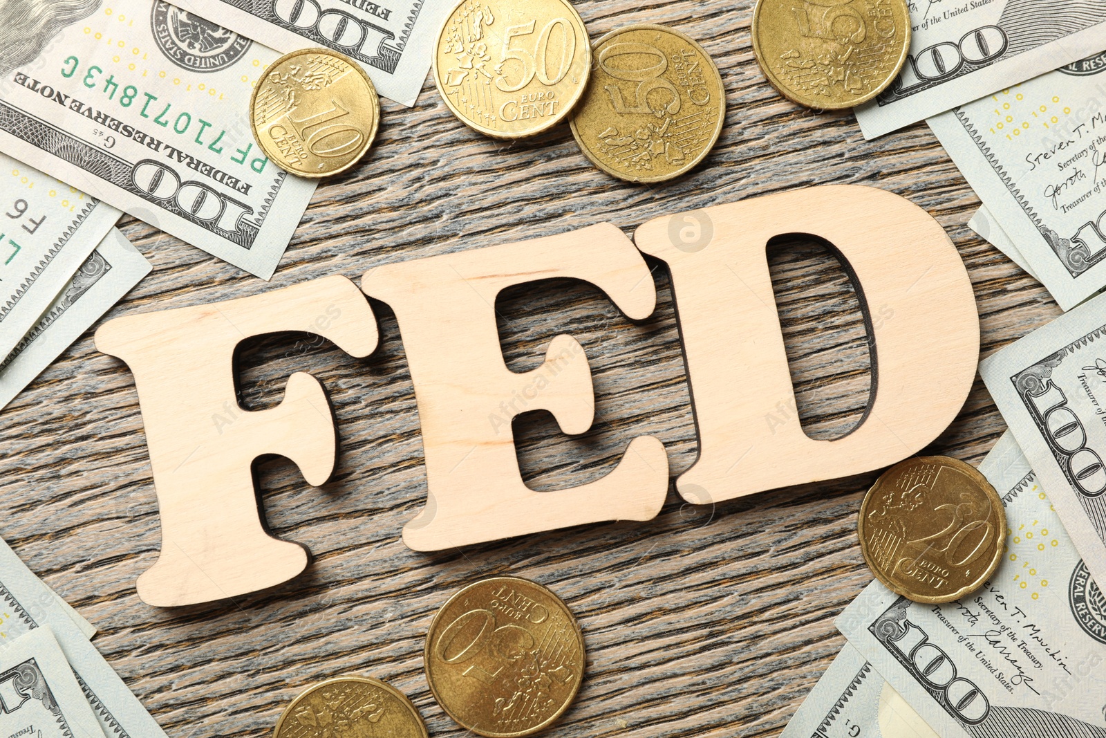 Photo of Letters Fed (Federal Reserve System), dollar banknotes and coins on wooden table, flat lay