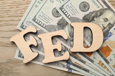 Photo of Letters Fed (Federal Reserve System) and dollar banknotes on wooden table, flat lay