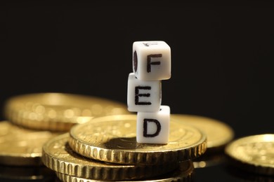 Photo of Cubes with letters Fed (Federal Reserve System) and coins on black table, closeup