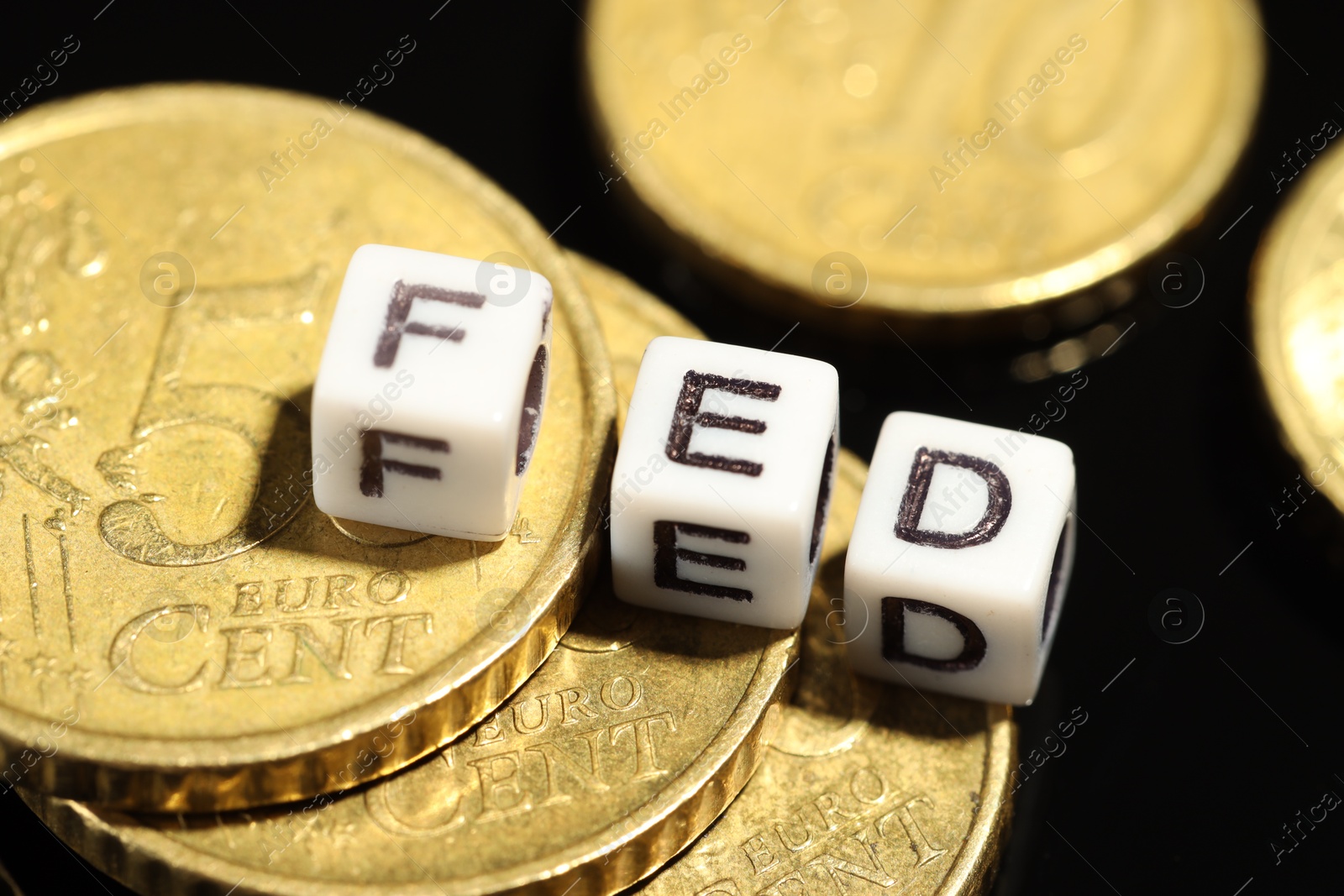 Photo of Cubes with letters Fed (Federal Reserve System) and coins on black table, closeup