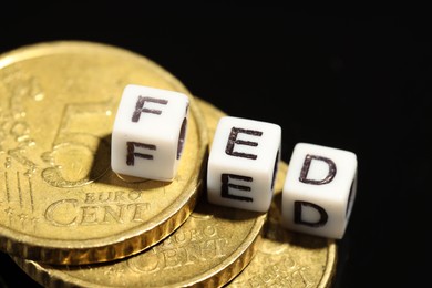 Photo of Cubes with letters Fed (Federal Reserve System) and coins on black table, closeup