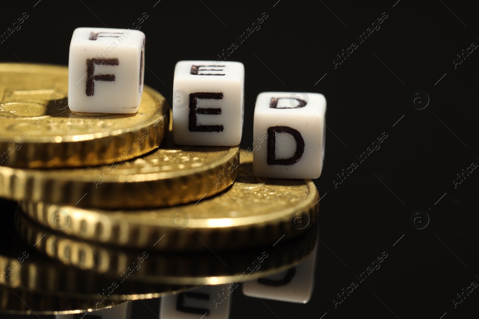 Photo of Cubes with letters Fed (Federal Reserve System) and coins on black table, closeup. Space for text