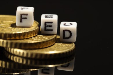 Photo of Cubes with letters Fed (Federal Reserve System) and coins on black table, closeup. Space for text