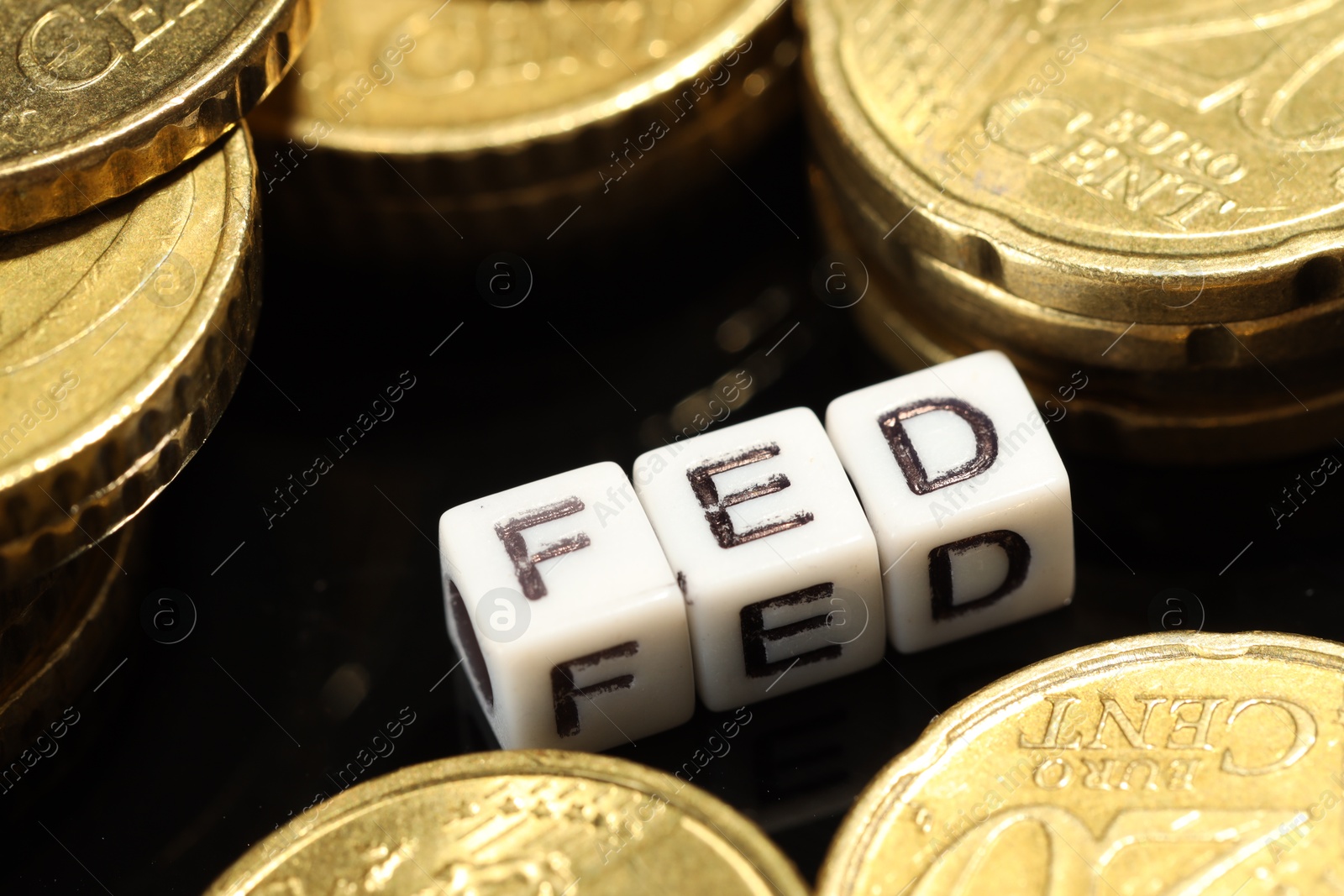 Photo of Cubes with letters Fed (Federal Reserve System) and coins on black table, closeup