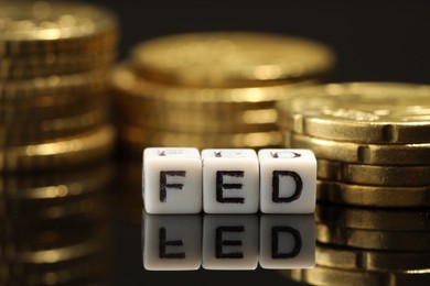 Photo of Cubes with letters Fed (Federal Reserve System) and coins on mirror table, closeup