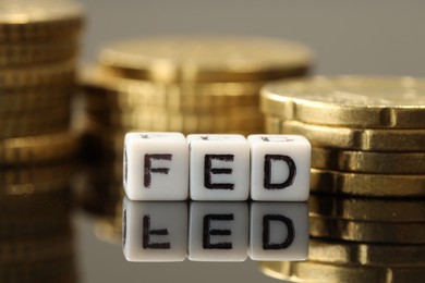 Photo of Cubes with letters Fed (Federal Reserve System) and coins on mirror table, closeup