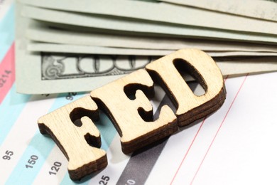 Photo of Wooden letters Fed (Federal Reserve System) and dollar banknotes on documents, closeup