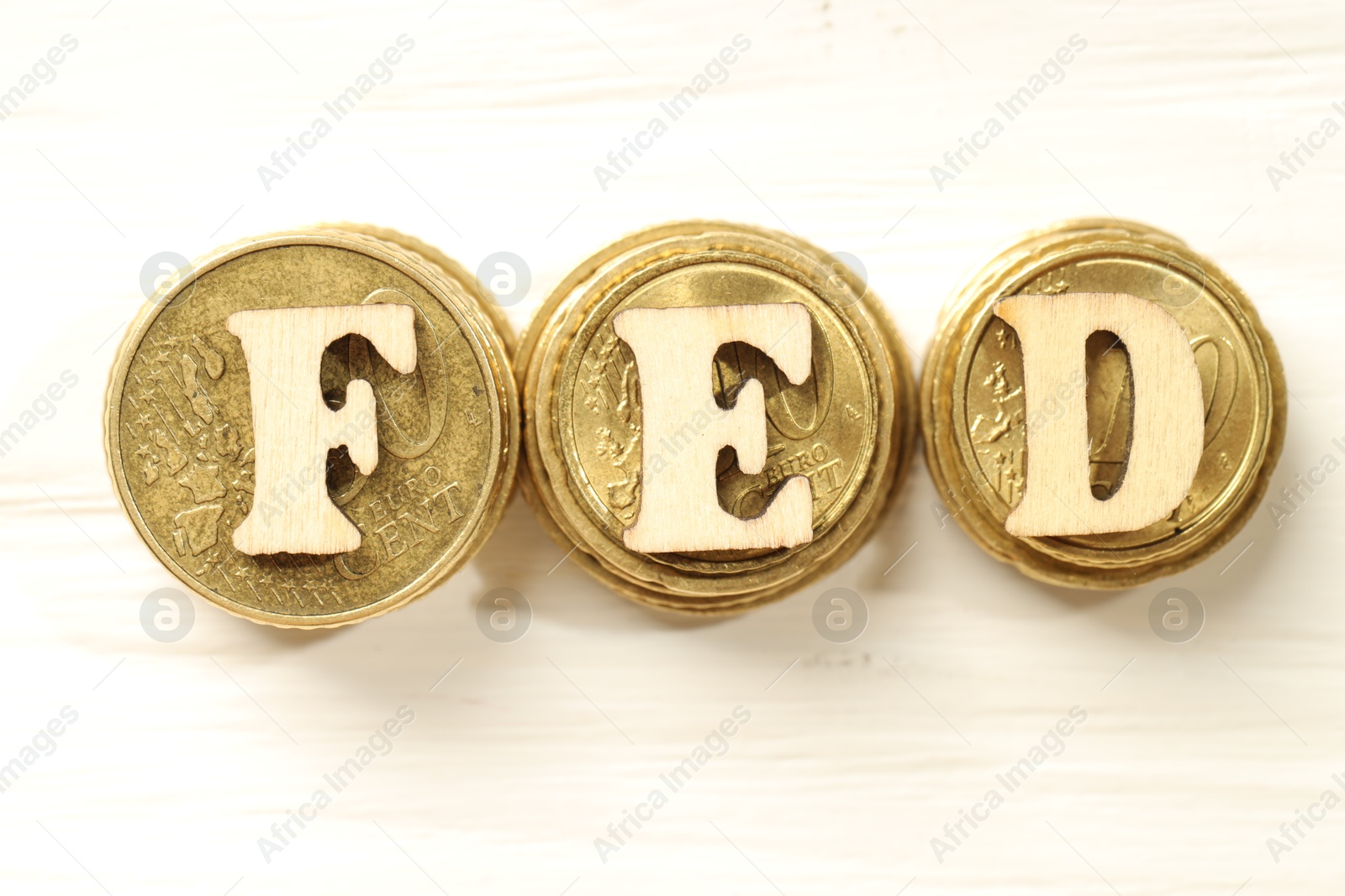 Photo of Wooden letters Fed (Federal Reserve System) and stacks of coins on white table, flat lay