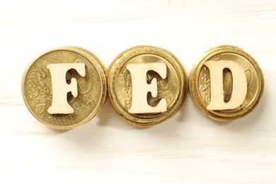 Photo of Wooden letters Fed (Federal Reserve System) and stacks of coins on white table, flat lay