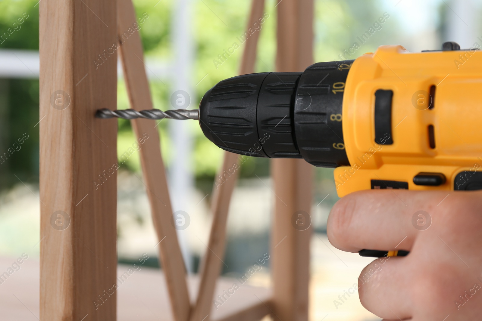 Photo of Man with electric screwdriver assembling furniture indoors, closeup