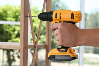 Man with electric screwdriver assembling furniture indoors, closeup