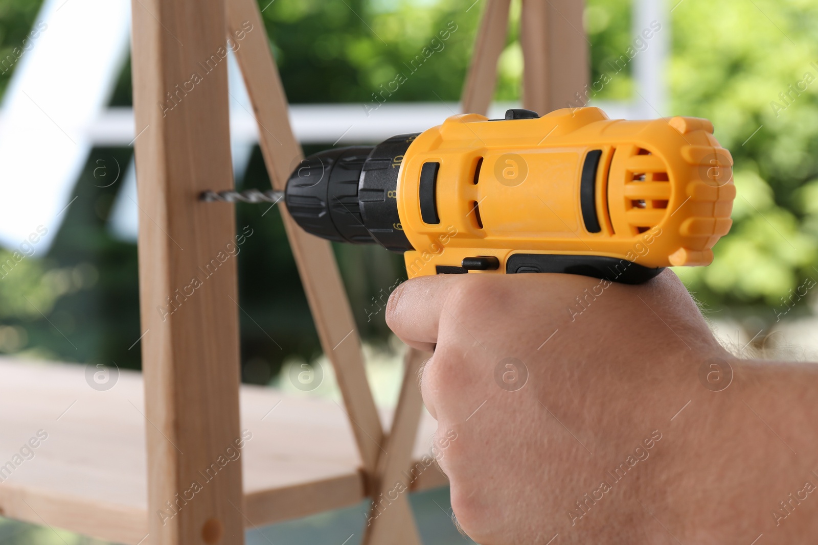 Photo of Man with electric screwdriver assembling furniture indoors, closeup