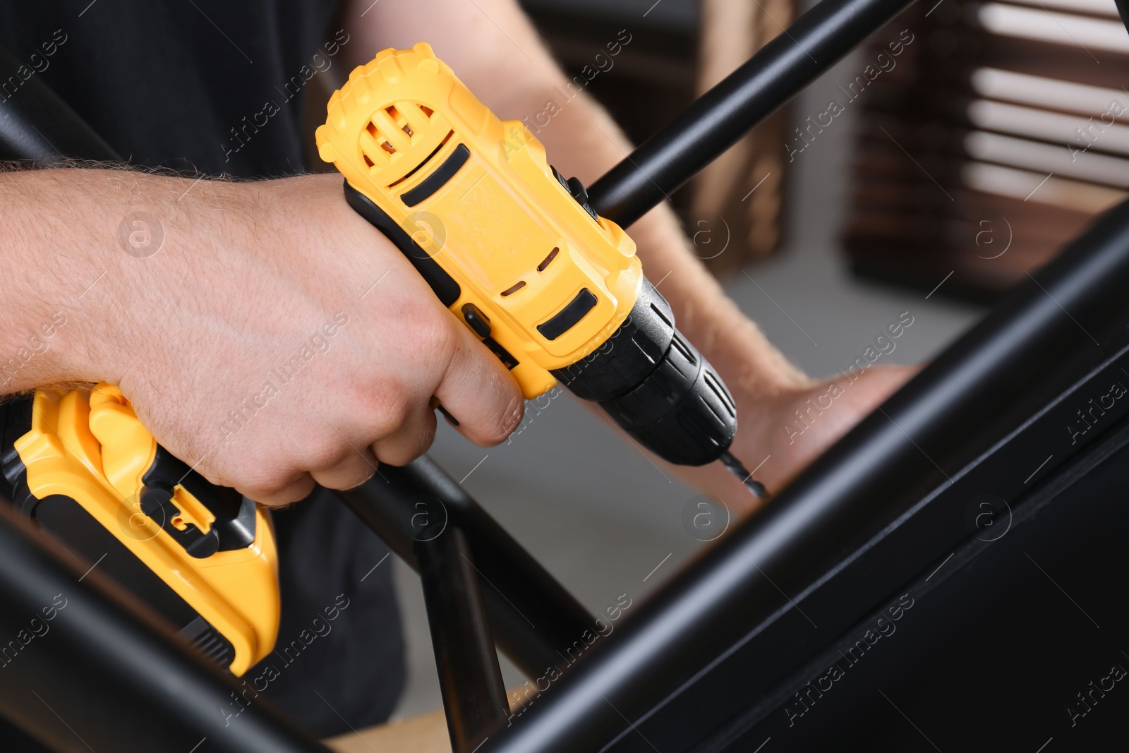 Photo of Man with electric screwdriver assembling furniture in room, closeup