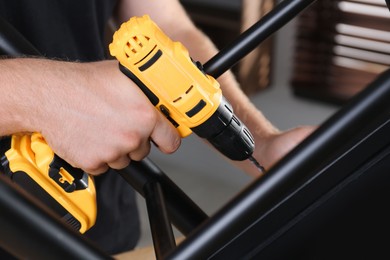 Man with electric screwdriver assembling furniture in room, closeup