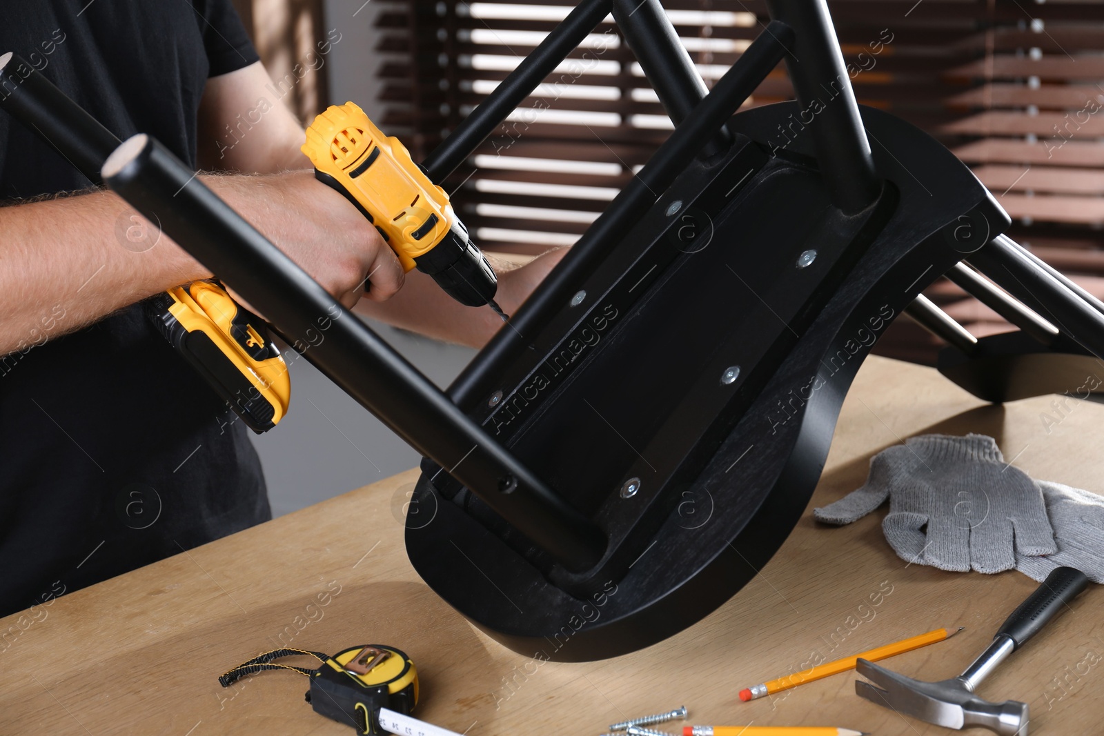 Photo of Man with electric screwdriver assembling chair in room, closeup